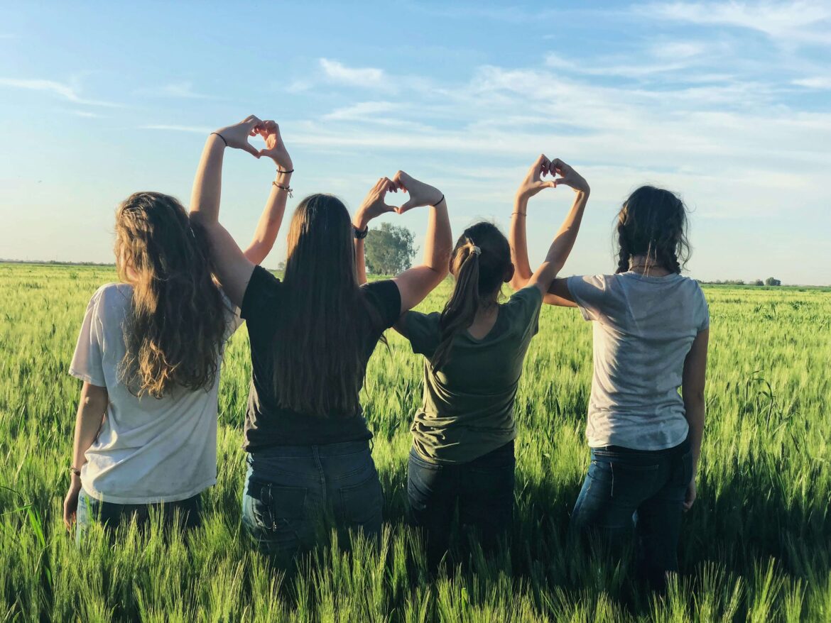 4 Frauen auf einer Wiese von hinten, die mit den Händen Herzen formen - Frauengesundheit